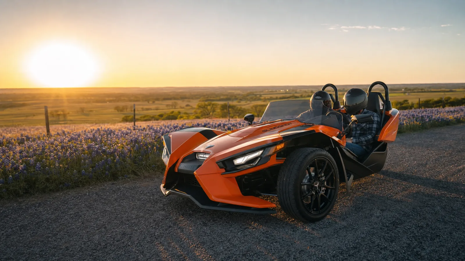 A vibrant orange Polaris Slingshot parked on a rural Texas farm road at golden hour, bluebonnet field alongside. Hero image for the Ennis Slingshot article "Polaris Slingshot 101: The First-Timer's Complete Guide"