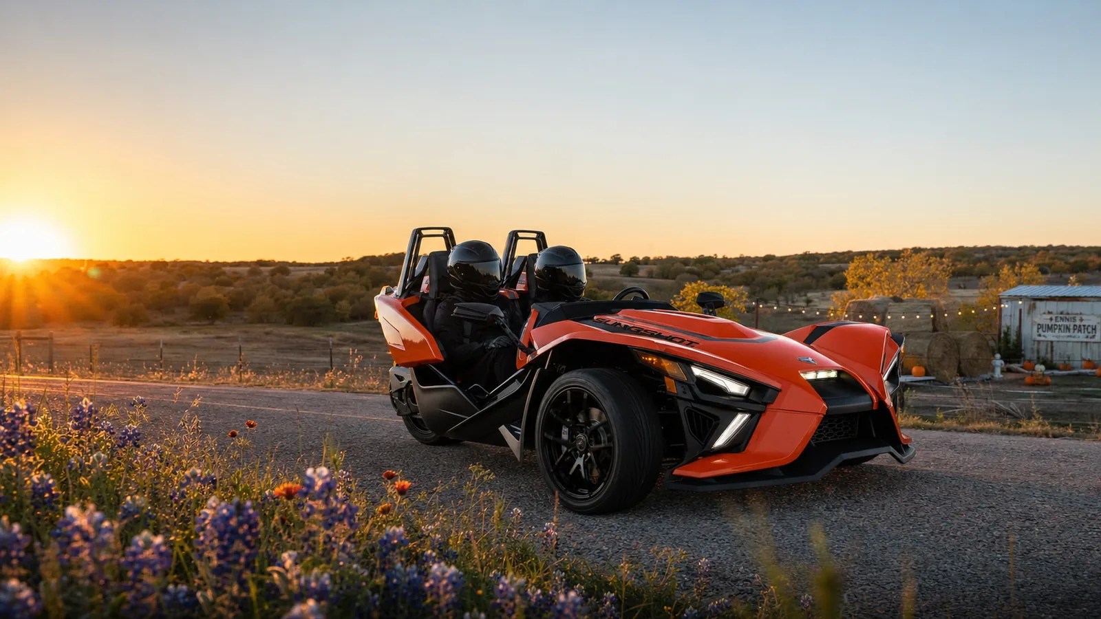An orange Polaris Slingshot on an autumn rural road near pumpkin patches and golden foliage at golden hour. Hero image for the Ennis Slingshot article "Fall in Ellis County: Pumpkin Patches, Festivals and Race Weekends"