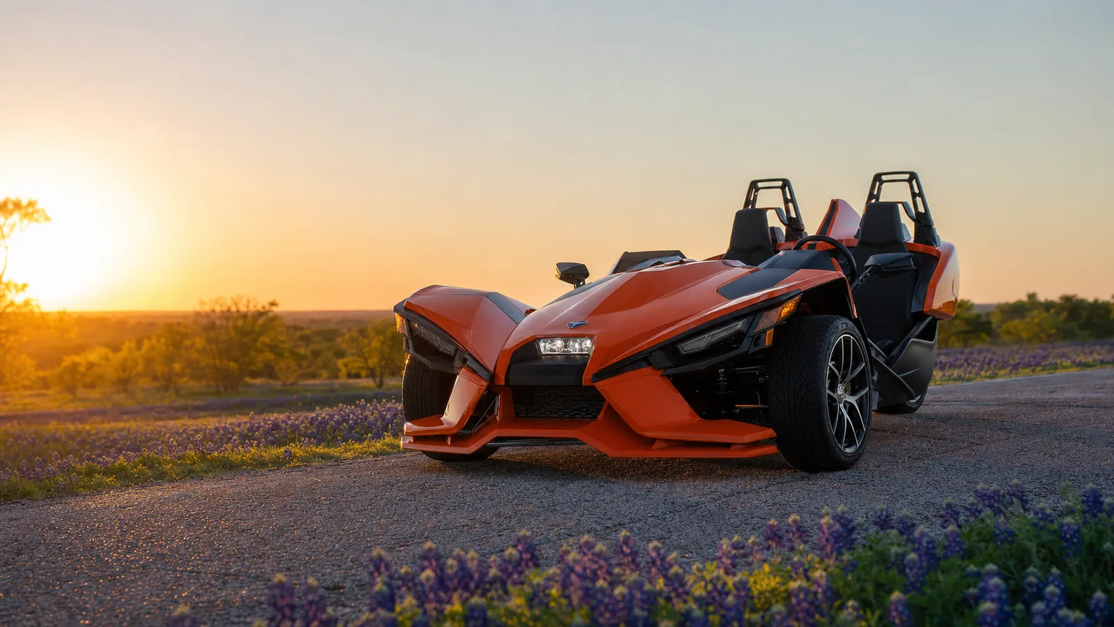 A close detail shot of the three-wheel layout and steering wheel of an orange Polaris Slingshot at golden hour. Hero image for the Ennis Slingshot article "What Is an Autocycle? The Three-Wheel Category the Slingshot Created"