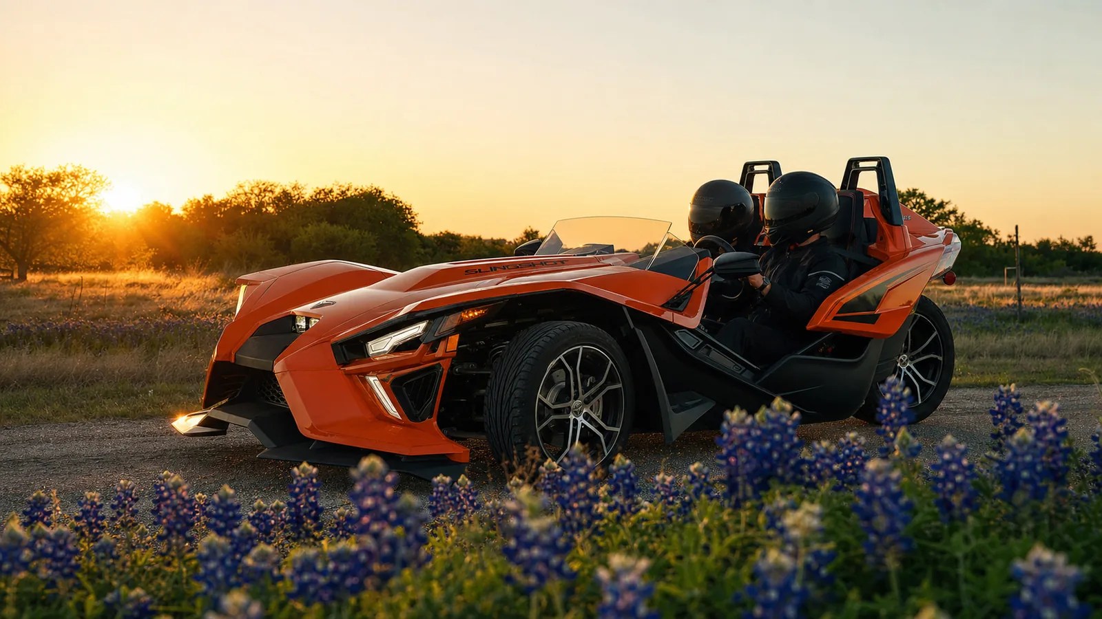 A helmeted driver settling into the driver's seat of an orange Polaris Slingshot at golden hour. Hero image for the Ennis Slingshot article "How Old Do You Have to Be to Drive a Polaris Slingshot? Law vs Rental Rules"