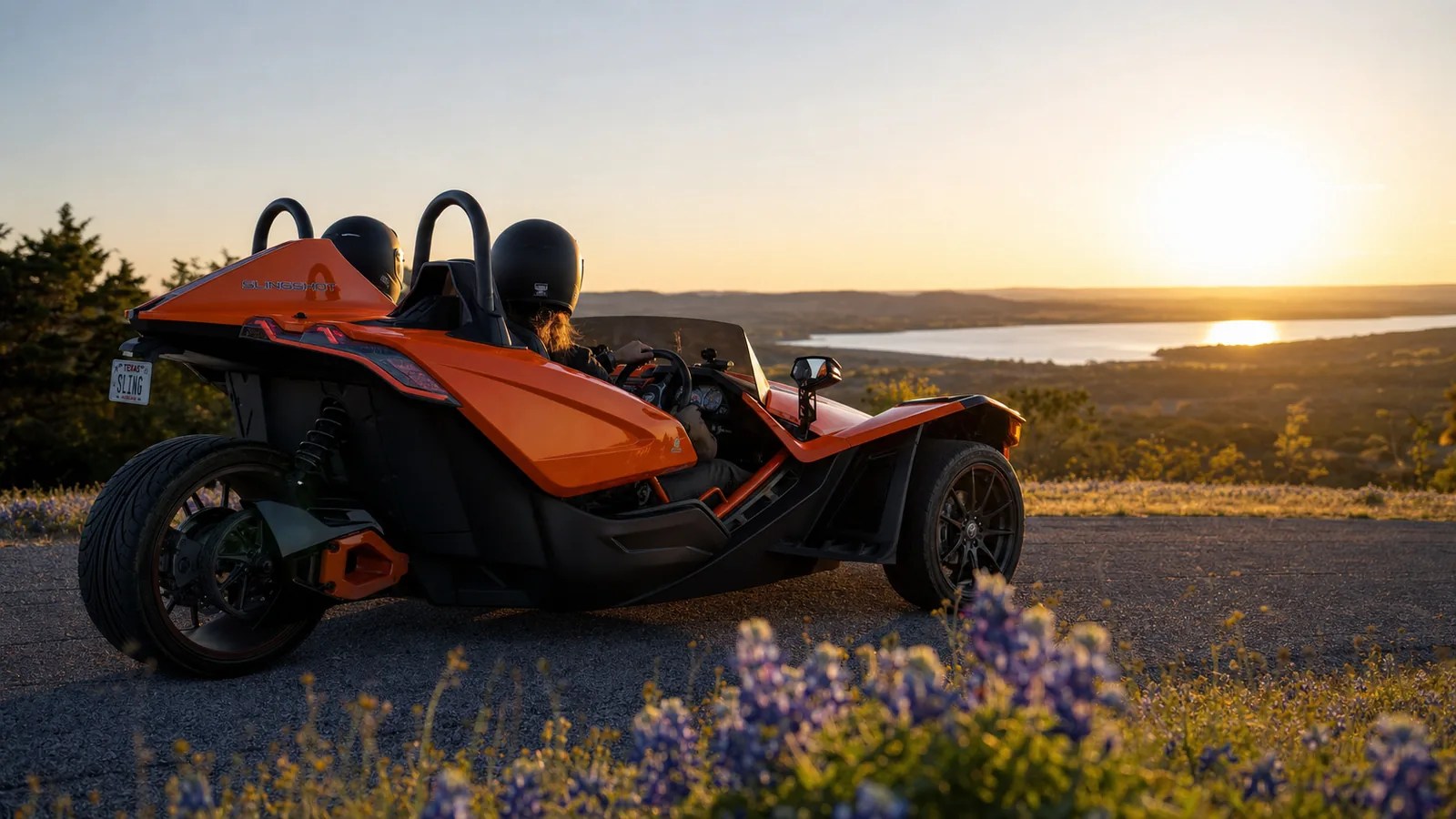 A couple in an orange Polaris Slingshot at a scenic overlook at golden hour. Hero image for the Ennis Slingshot article "Outdoor Date Ideas Near Dallas: A Season-by-Season Guide"