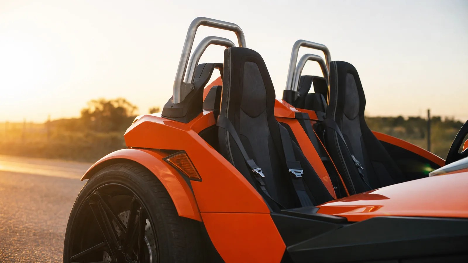 A detail of the roll hoop, seat belts and front wheel of an orange Polaris Slingshot at golden hour. Hero image for the Ennis Slingshot article "Polaris Slingshot Safety Features Explained: ABS, Stability Control, Belts and the Roll Hoop"
