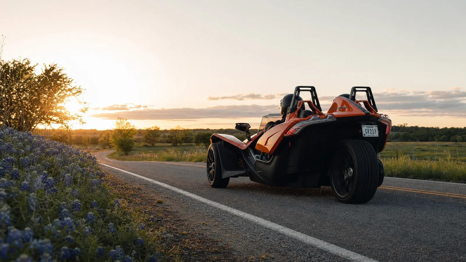 An orange Polaris Slingshot on a quiet Texas back road at golden hour. Hero image for the Ennis Slingshot article "The Motorcyclist Who Found These Roads: Our Story, and Why It's an Experience, Not a Rental"