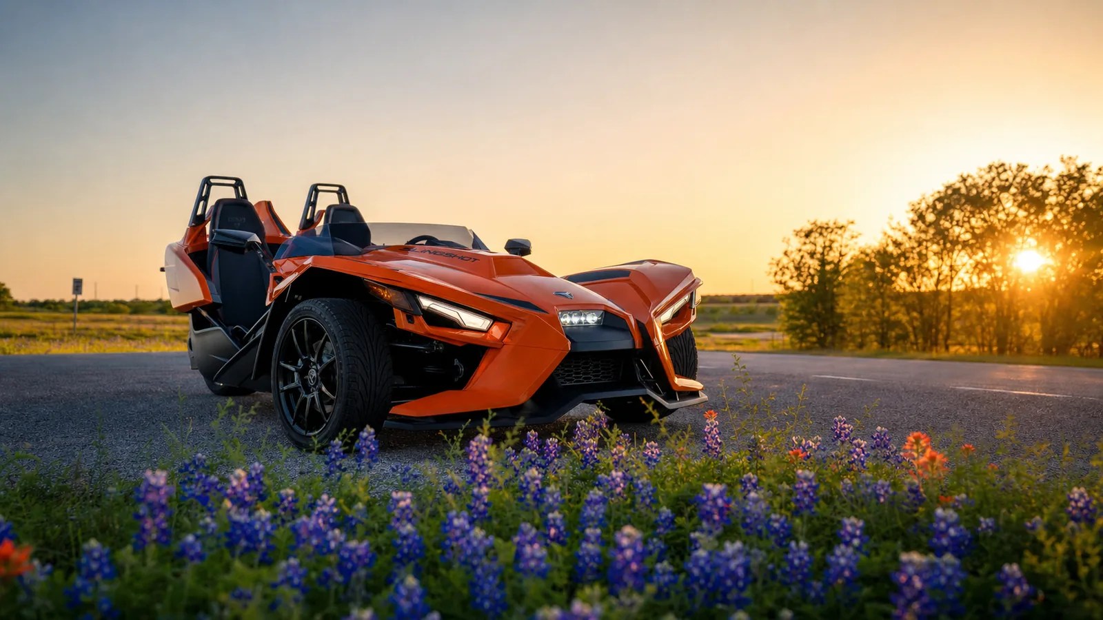 An orange Polaris Slingshot parked at a scenic Texas spot at golden hour. Hero image for the Ennis Slingshot article "Birthday Ideas in Dallas for Adults: Ways to Celebrate"