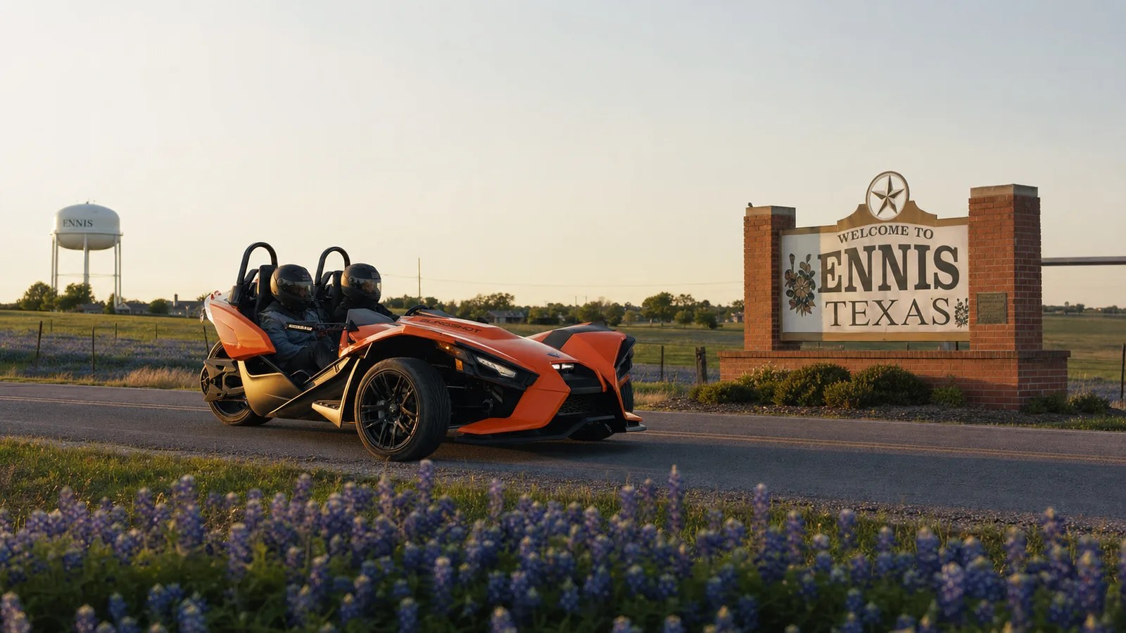 An orange Polaris Slingshot on a bluebonnet road near Ennis at golden hour. Hero image for the Ennis Slingshot article "How Ennis Became the Official Bluebonnet City of Texas: The 1997 Legislature Story"