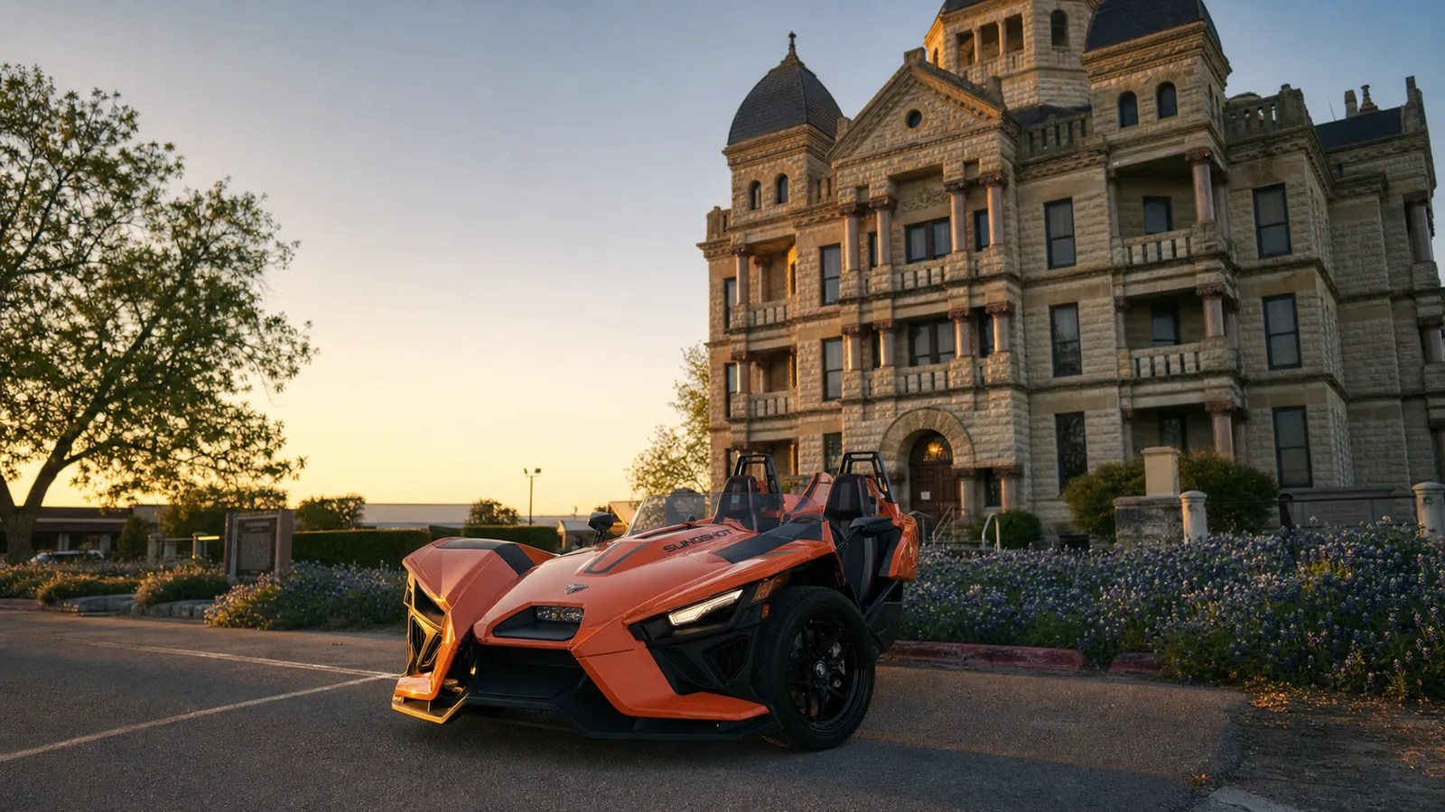 An orange Polaris Slingshot parked in front of a historic Texas courthouse at golden hour. Hero image for the Ennis Slingshot article "Things to Do in Waxahachie, TX (Courthouse to Gingerbread Houses)"
