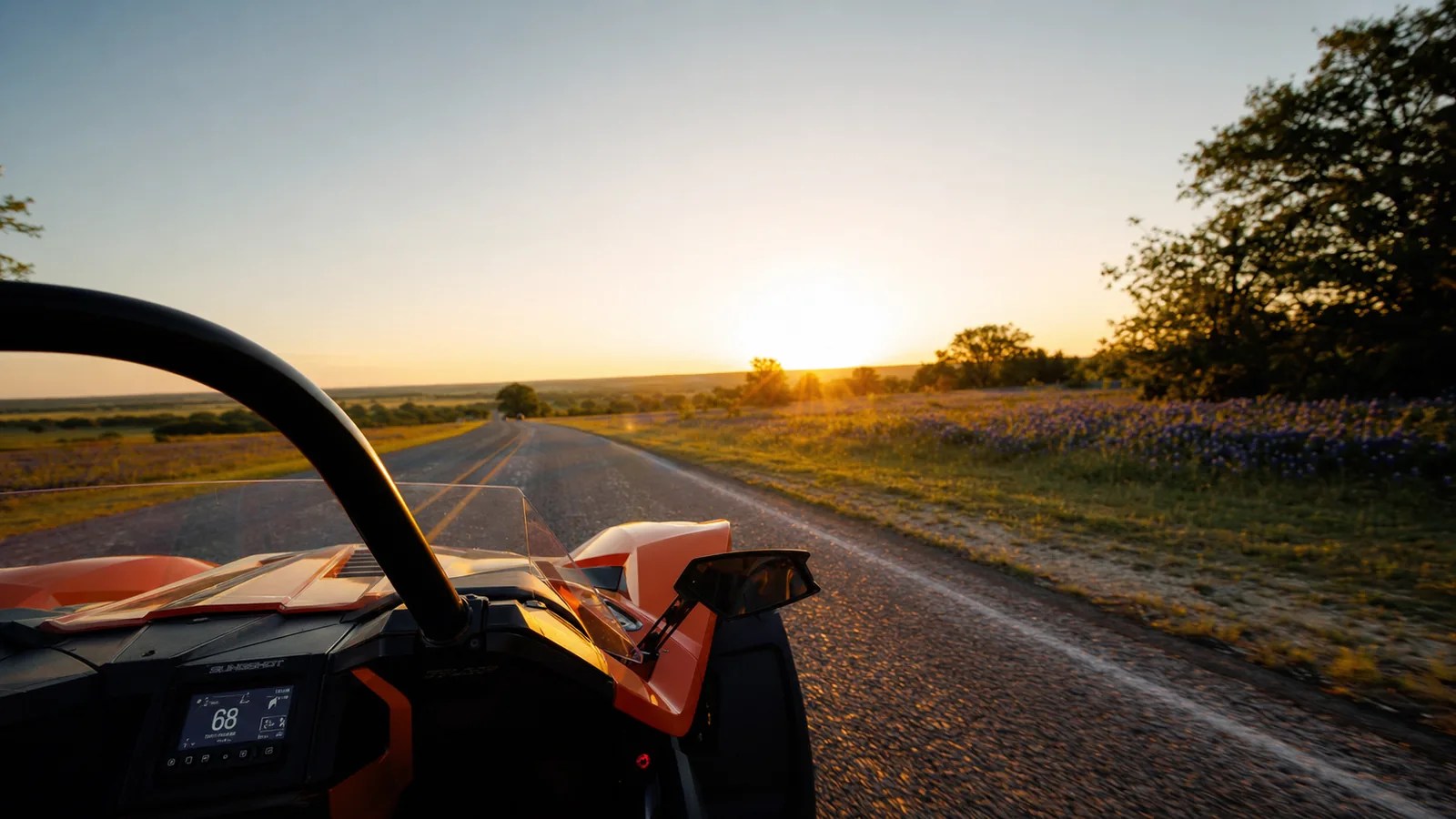 A passenger's view from an orange Polaris Slingshot looking out over a Texas country road at golden hour. Hero image for the Ennis Slingshot article "Riding as a Passenger in a Slingshot: The Two-Up Guide"
