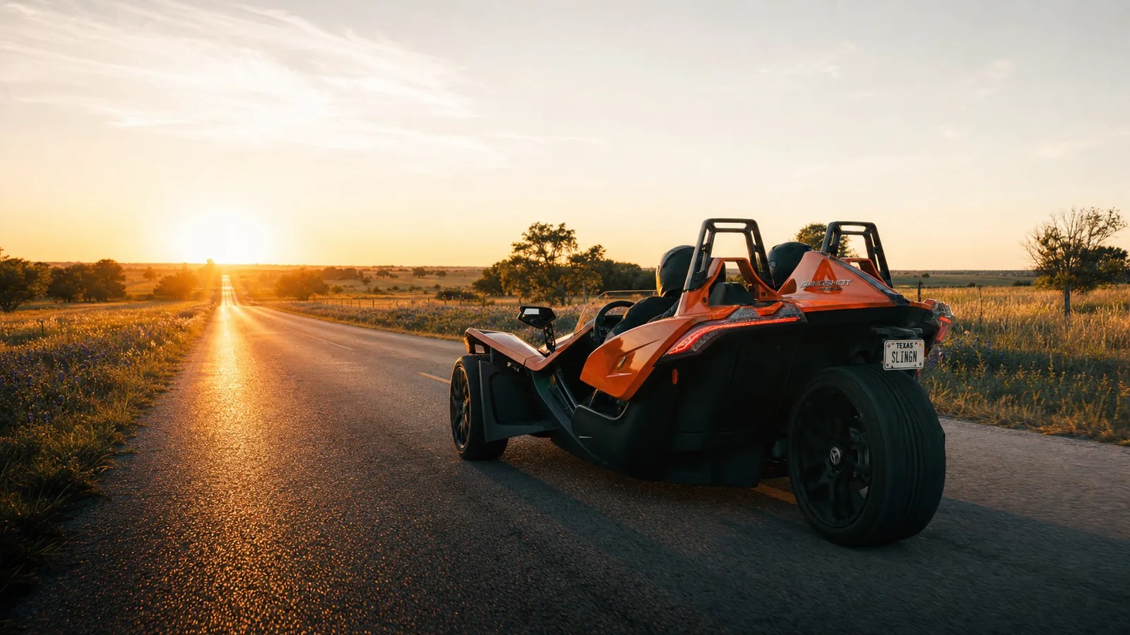 An orange Polaris Slingshot on a long open Texas road at golden hour. Hero image for the Ennis Slingshot article "Polaris Slingshot Top Speed: What It Will Really Do (By Trim)"