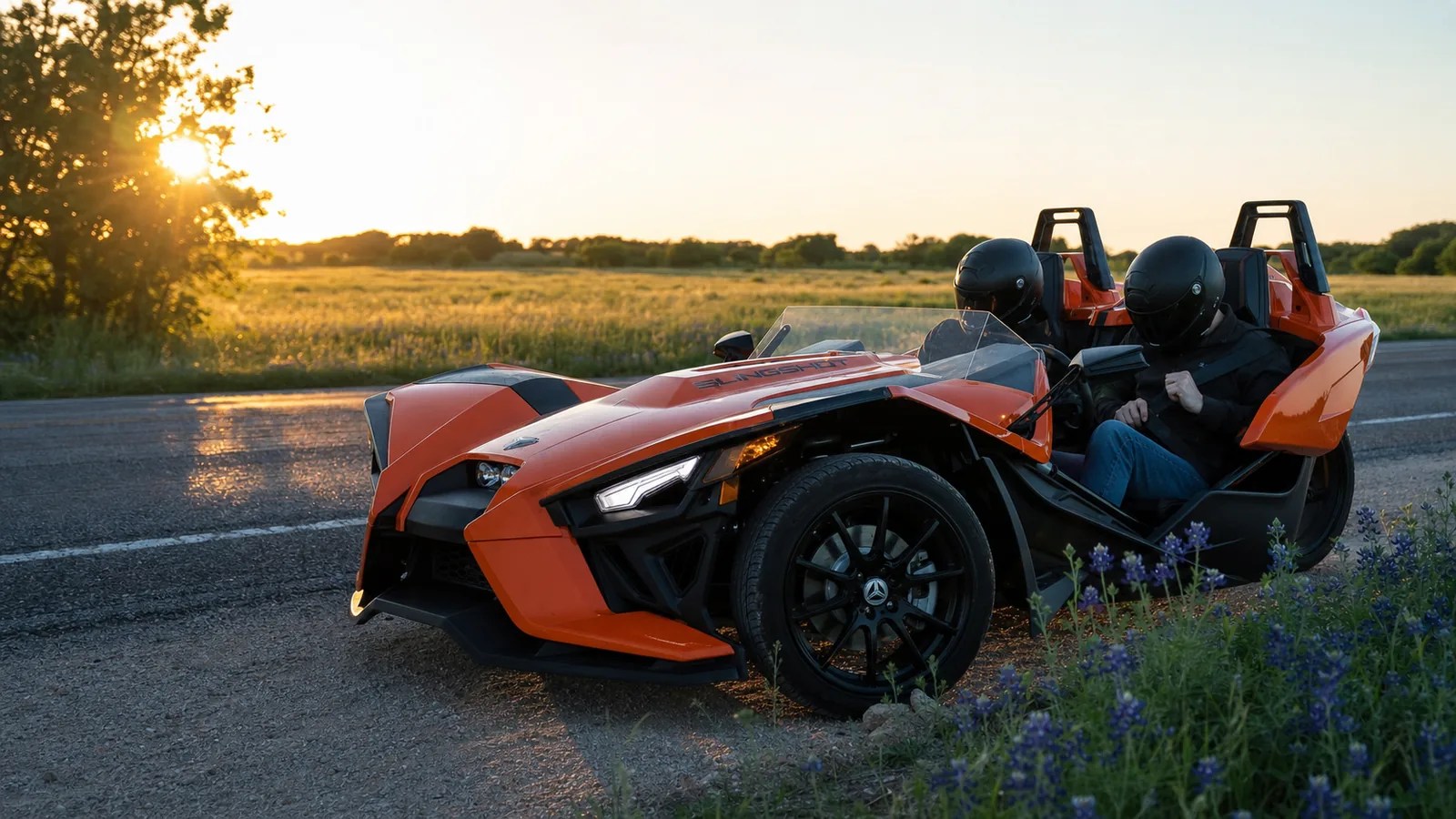 An adult driver buckling the seat belt of an orange Polaris Slingshot at golden hour. Hero image for the Ennis Slingshot article "Can Kids Ride in a Polaris Slingshot? Texas Rules and Operator Policies"