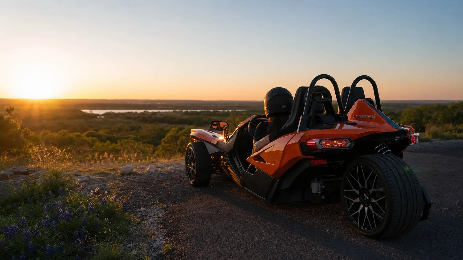 A couple in an orange Polaris Slingshot at a scenic pull-off at sunset. Hero image for the Ennis Slingshot article "Anniversary Ideas in Dallas: Dates Worth Remembering"