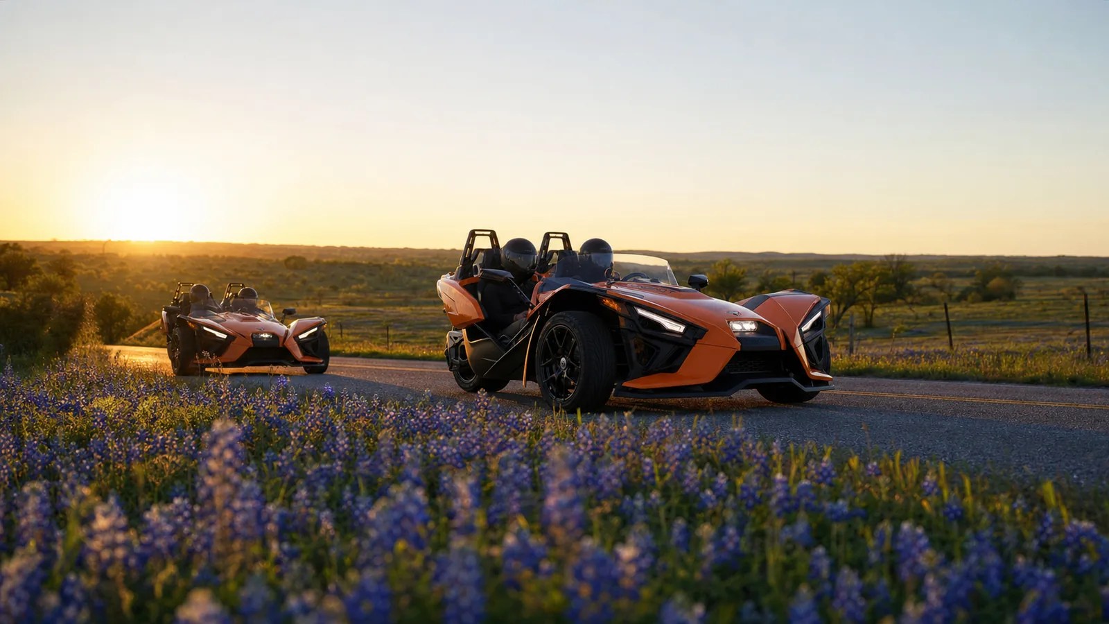 Two orange Polaris Slingshots driving in convoy on a Texas road at golden hour. Hero image for the Ennis Slingshot article "Fun Things to Do With Friends in Dallas: Ideas for a Group of 3 or 4"