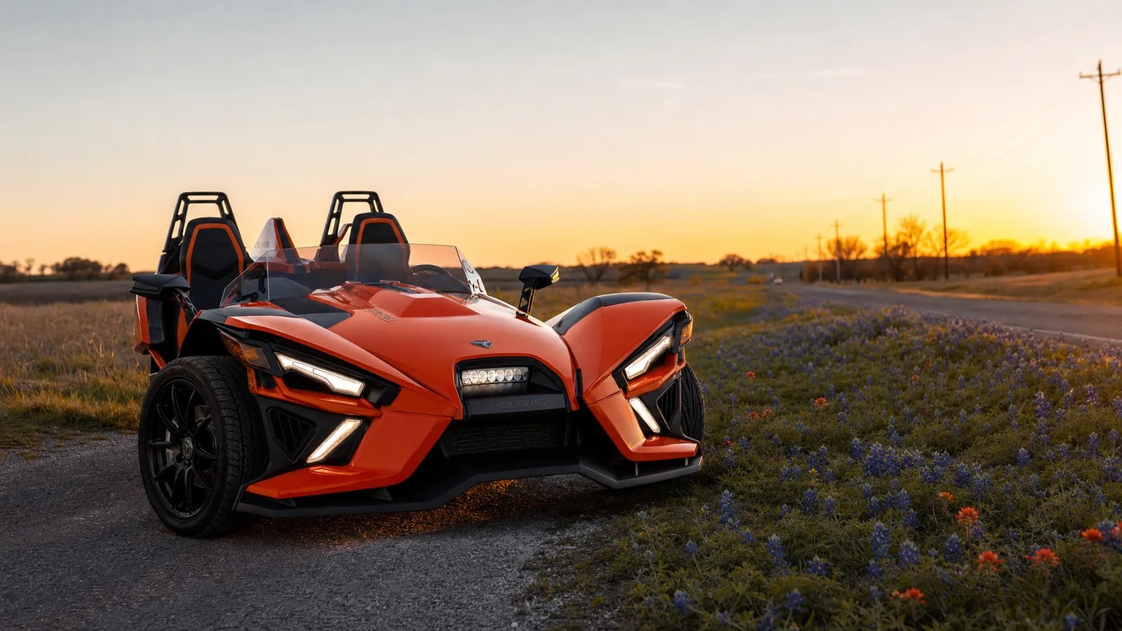 An orange Polaris Slingshot shown in a front three-quarter view at golden hour. Hero image for the Ennis Slingshot article "2026 Polaris Slingshot Specs by Trim: S, SL, SLR, R, Signature and Grand Touring"